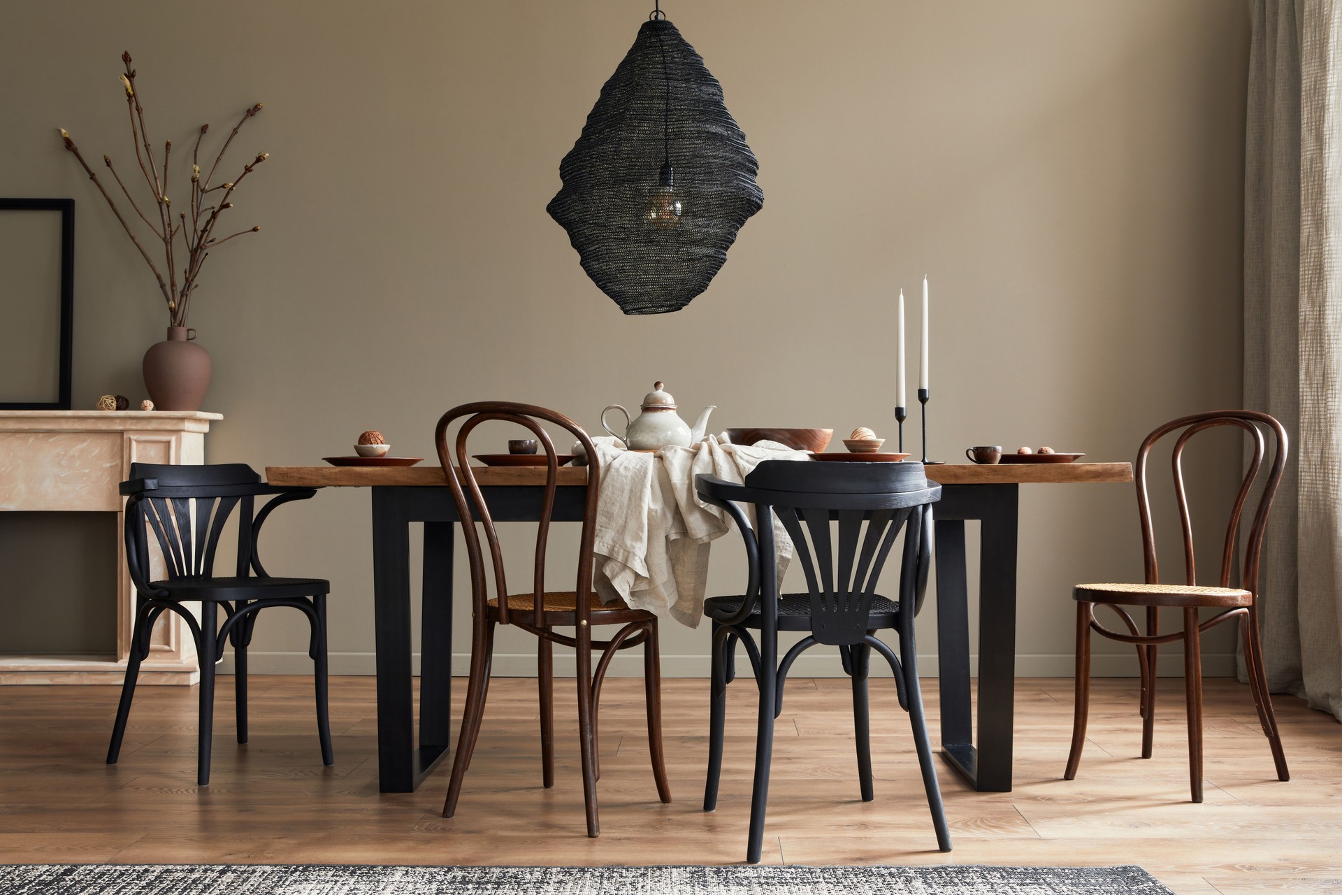 Stylish rustic interior of dining room with walnut wooden table, retro chairs, pedant lamp, fireplace, dried flower, candlestick mock up picture frame and carpet in minimalist home decor. Template.